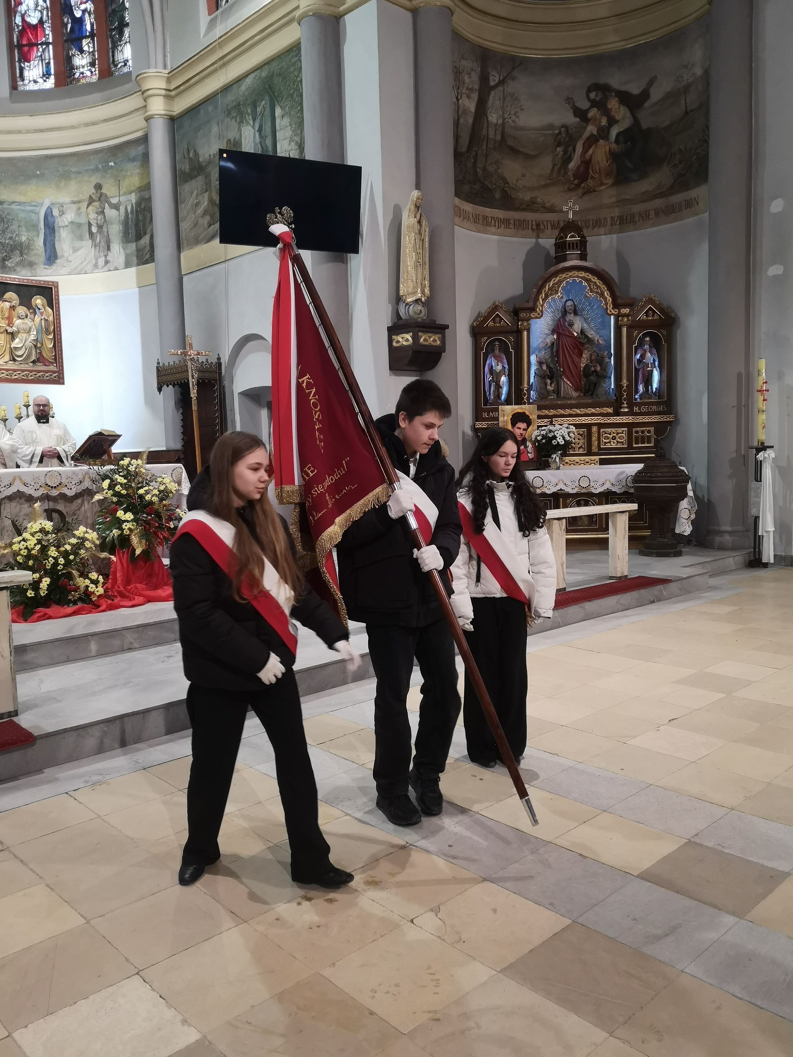 Uczniowie w kościele niosą sztandar szkoły.