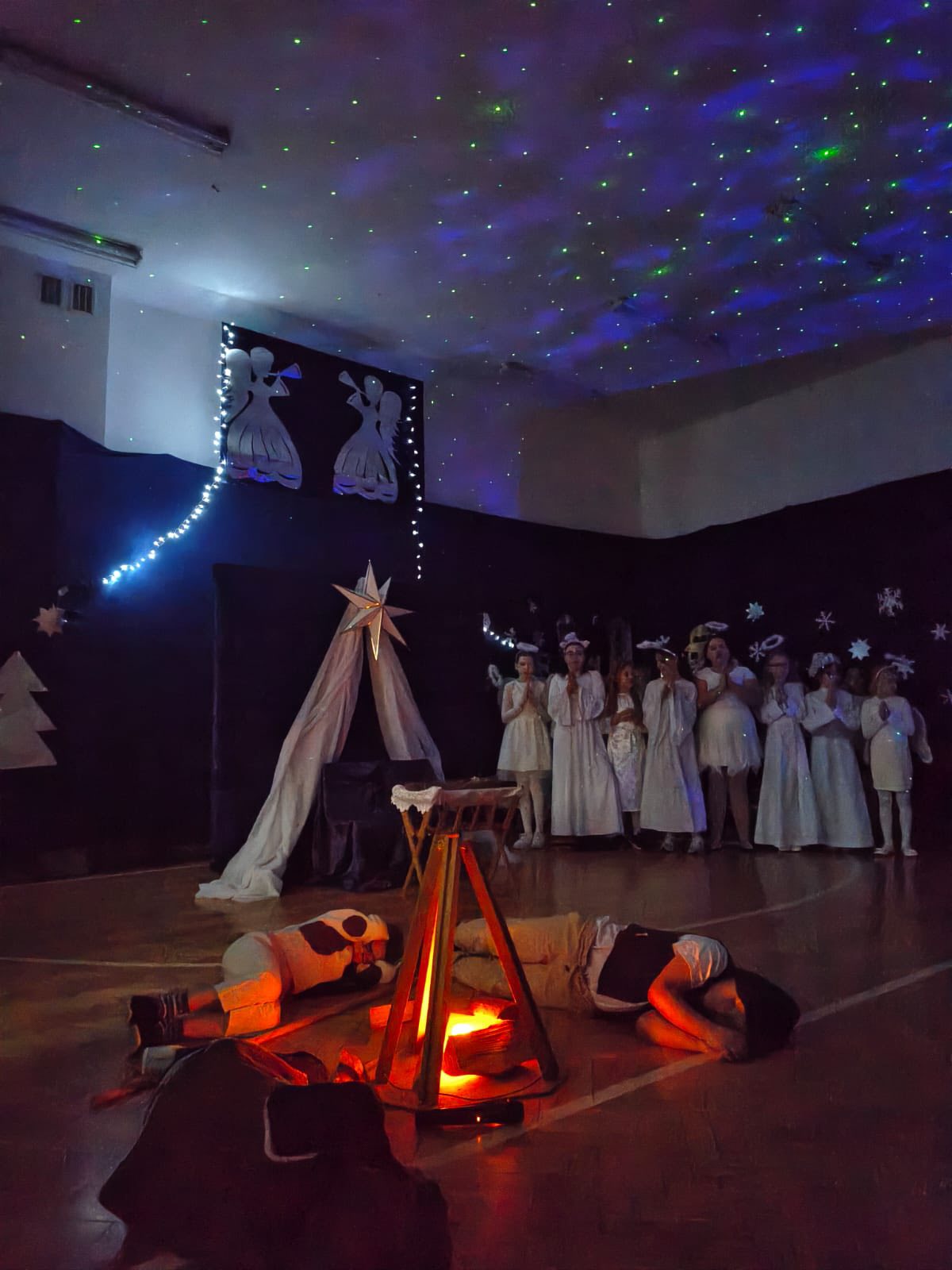 Zdjęcie przedstawiające noc, stajenkę betlejemską i śpiących przy ognisku pasterzy i chór aniołów